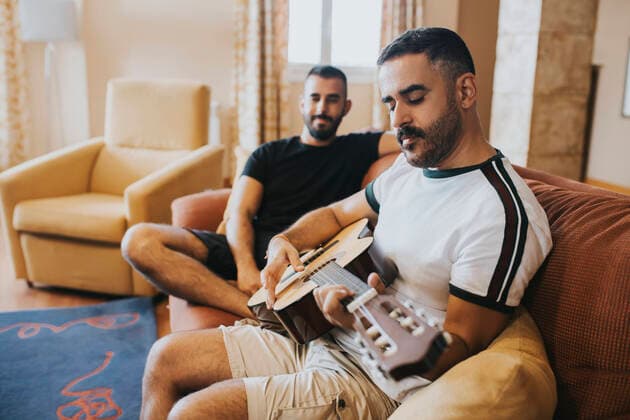 Creative Highlights Symbolbilder Gay boy watches his boyfriend playing the guitar on the sofa Almería, AL, Spain CR_QYWX200623B-425176-01 ,model released, Symbolfoto