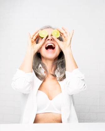 Creative Highlights Symbolbilder Happy mature woman holding lemons over eyes sitting in front of wall model released, Symbolfoto, JBYF00198