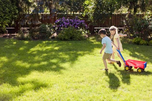 IMAGO Creative: Sommer, Sommertage im Garten Playful girl pulling toy wagon with brother on sunny day in back yard model released, Symbolfoto, ONAF00313