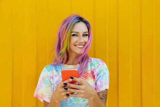 Happy young woman holding mobile phone in front of yellow wall model released, Symbolfoto property released, SYEF00109