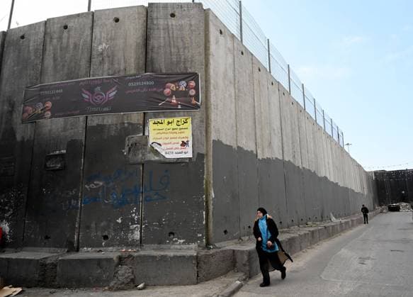 A Palestinian walks beside the Israeli separation wall that surrounds the Shuafat Refugee Camp in Jerusalem on Tuesday, January 3, 2023.  JER2023010309 DEBBIExHILL