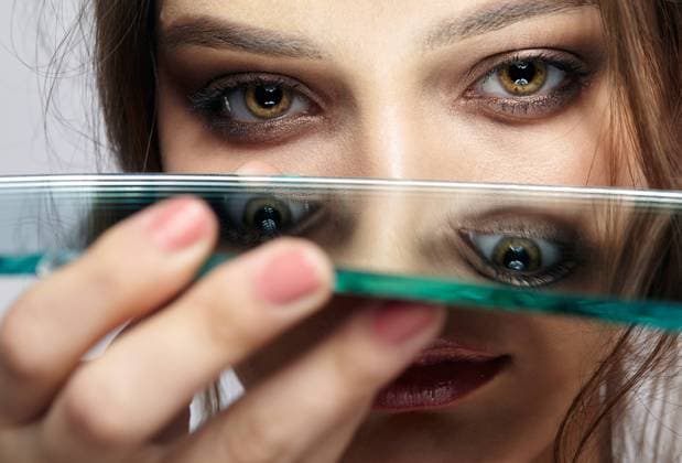 Portrait of a beautiful girl with a mirror splinter near eyes. Portrait of a beautiful girl with a mirror splinter near eyes. Female with mirror shard in hand posing on gray background. Copyright: xZoonar.com SergxZastavkinx(SergeyxPristyazhnyuk)x 15063137 ,model released, Symbolfoto ,property released