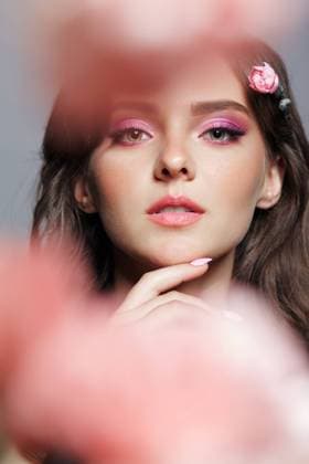 Beauty portrait of young woman with front bokeh of pink flower petals. Beauty portrait of young woman on gray background. Front bokeh of pink flower petals. Hand near face. Copyright: xZoonar.com SergeyxPistyazhnyukx(SergxZastavkin)x 17682549 ,model released, Symbolfoto ,property released