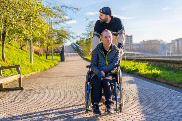 Lächelnde behinderte Person im Rollstuhl, die mit ihrem Bruder in einem Park spazieren geht *** smiling Disabled Person at Wheelchair, the with their Brother in a Park walk goes Copyright: imageBROKER/UnaixHuizi ibxuhu08962877.jpg ,model released, Symbolfoto ,property released