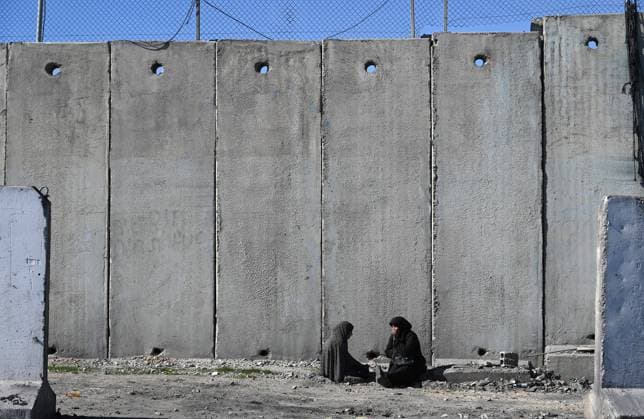 Palestinian peddlers rest by the Israeli separation wall at the Qalandiya Checkpoint, between Jerusalem and Ramallah, in the West Bank, on Thursday, January 19, 2023.  JER2023011906 DEBBIExHILL
