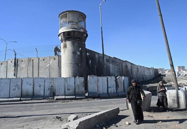 Palestinians walk past a military guard tower in the separation wall at the Israeli controlled Qalandiya Checkpoint, between Jerusalem and Ramallah, in the West Bank, on Thursday, January 19, 2023.  JER2023011908 DEBBIExHILL