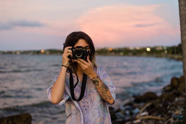 Young woman in glasses and casual clothes standing against rippling sea water and sunset sky in Cuba while taking a photo with her camera, Model released, Property released AlbaCaro_ID8062_242694_063 Copyright: xAlbaxCarox MR