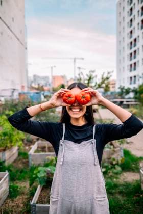 Happy young woman holding tomatoes over eyes in urban garden model released, Symbolfoto, GDBF00035