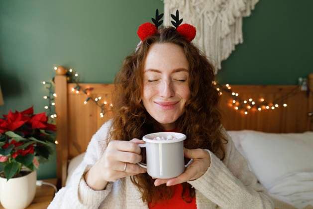 Smiling woman with eyes closed holding cup of hot chocolate on bed at home model released, Symbolfoto property released, TYF00656