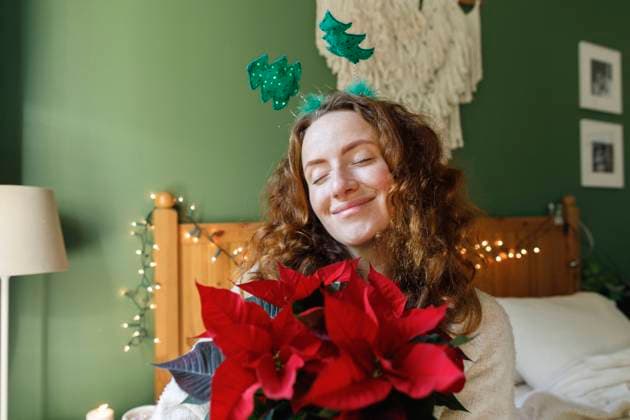 Smiling woman with eyes closed holding Poinsettia plant at home model released, Symbolfoto property released, TYF00658