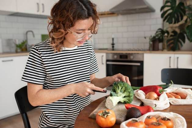 Woman cutting vegetable sitting on table at home model released, Symbolfoto property released, VRAF00053