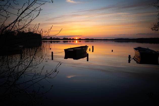 IMAGO Creative, Jahreszeit Frühling, Licht und Sonne a colorful sunset on a lake with a boat on the shore