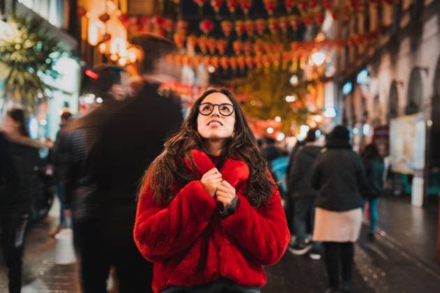 Positive young female in warm clothes and eyeglasses smiling while looking up at lanterns and admiring London city street at night, Model released PabloMenendez_ID12632_384115_003 Copyright: xPabloxMenendezx MR