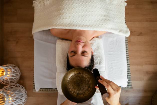 Top view of crop anonymous traditional medicine doctor playing Tibetan singing bowl over head of relaxed female client lying on table with closed eyes during meditation session AidaMartinez_ID12552_381113_068 Copyright: xAidaxMartinezx Model Released