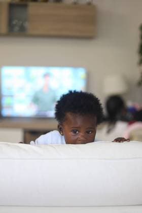 Creative Highlights Symbolbilder Adorable African American baby hiding behind pillow while looking away in living room, Model released Gaorstudio_ID12713_385874_003 Copyright: xGaorstudiox MR