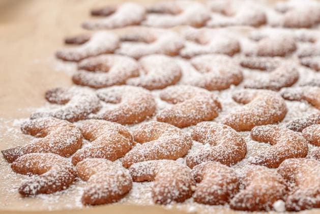 Vanillekipferl auf einem Backblech Background of traditional crescent shaped Christmas cookies or biscuits with crisp golden pastry sprinkled with sugar on a kitchen counter Copyright: xZoonar.com LarsxZahnerx 6592401