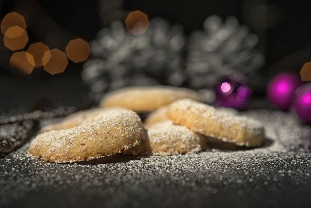 Traditionelle Vanillekipferl dekoriert zu Weihnach Freshly baked festive golden crescent cookies for Christmas and Advent sprinkled with icing sugar on a grey kitchen counter with Xmas decorations behind and shallow dof Copyright: xZoonar.com LarsxZahnerx 6601646