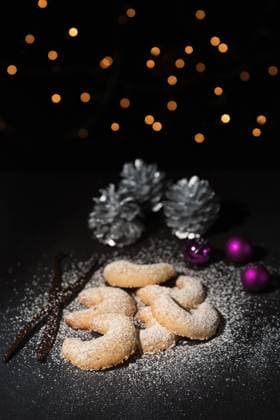 Traditionelle Vanillekipferl dekoriert zu Weihnach Freshly baked festive golden crescent cookies for Christmas and Advent sprinkled with icing sugar on a grey kitchen counter with Xmas decorations behind and shallow dof Copyright: xZoonar.com LarsxZahnerx 6601660
