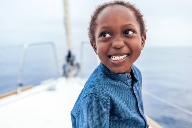 Creative Highlights Symbolbilder Positive African American boy in casual shirt smiling and looking away while sitting on yacht against sea, Model released AlfonsoSaenz_ID12778_387457_041 Copyright: xAlfonsoxSaenzx MR