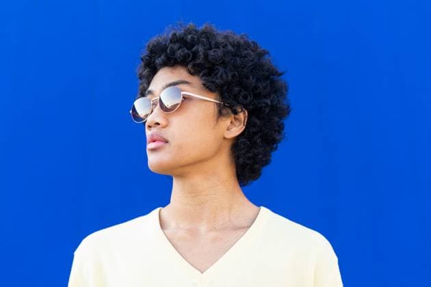 Serious young male in yellow sweatshirt and sunglasses with curly hair looking away while standing against bright blue wall, Model released DavidMunoz_ID12930_392761_035 Copyright: xDavidxMunozx MR