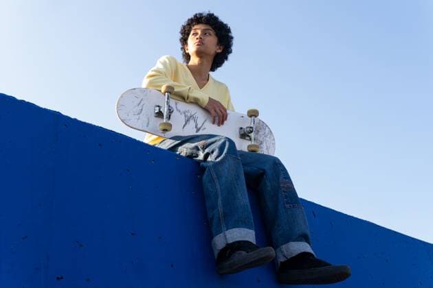 Creative Highlights Symbolbilder From below full body of serious young Asian male with curly hair skater in casual clothes sitting on blue ramp with skateboard and looking away, Model released DavidMunoz_ID12930_392806_073 Copyright: xDavidxMunozx MR