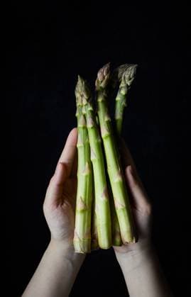 Crop anonymous hands of person showing bunch of fresh green asparagus against black background GeorgiaGold_ID12870_391172_002 Copyright: xGeorgiaxGoldx Model Released