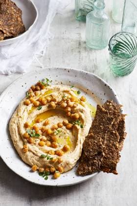 IMAGO Creative, Food, Hummus Top view of delicious hummus with chickpeas seeds and olive oil served on plate with crispy healthy crackers on table in kitchen GeorgiaGold_ID12873_391219_002 Copyright: xGeorgiaxGoldx Model Released