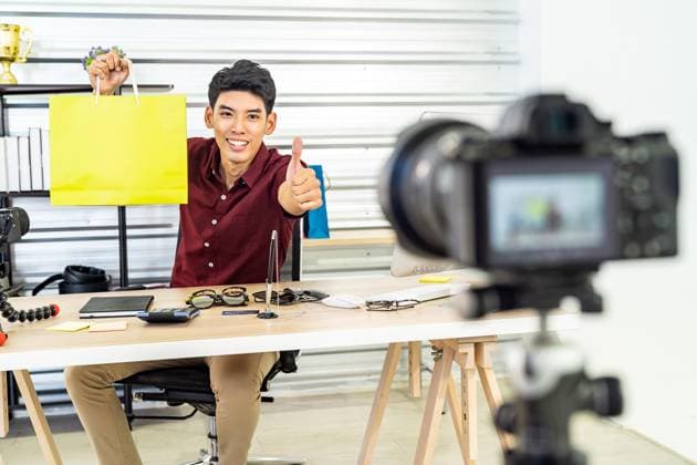 Online Merchant vlog live Young asian male online merchant blogger recording live vlog video with colorful shopping bag preparing for sale and review goods at home. Online influcencer on social media concept. Copyright: xZoonar.com Vichie81x 15210185 ,model released, Symbolfoto ,property released