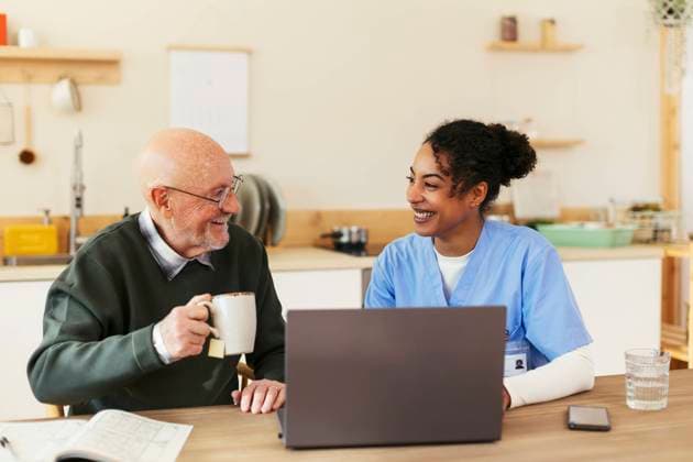 Happy senior man and caretaker sitting in front of laptop at home model released, Symbolfoto property released, EBSF02700