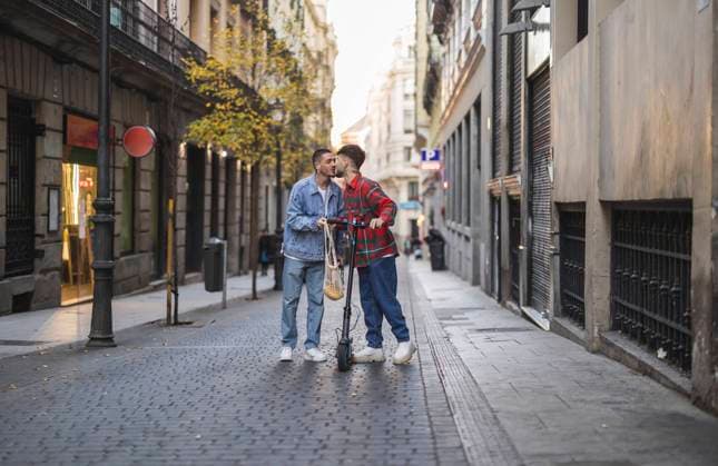 IMAGO Creative, Urban Lifestyle Happy gay couple kissing with electric push scooter amidst buildings model released, Symbolfoto property released, JCCMF09174