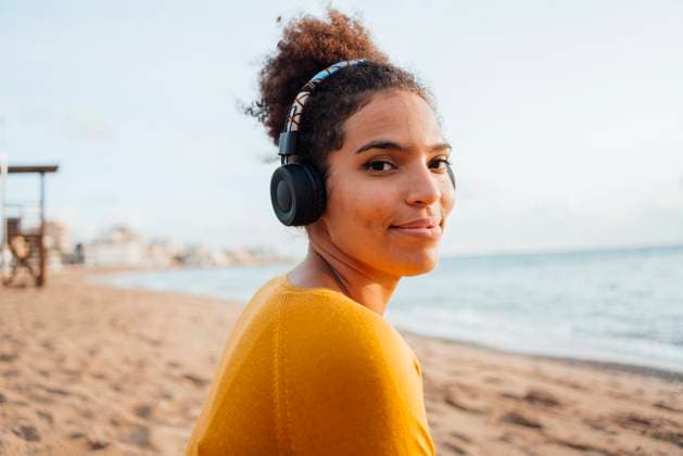 Smiling young woman wearing headphones listening to music at beach model released, Symbolfoto, JOSEF15861