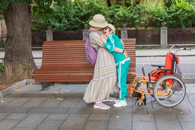 Mother embracing daughter with disability standing near bench model released, Symbolfoto, OSF01374