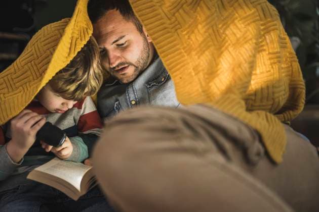 Father and son with torch reading book under yellow blanket model released, Symbolfoto property released, UUF28146