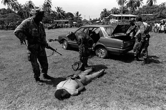 RECORD DATE NOT STATED A Marine armed with an M16A1 rifle stands guard over a captured member of the Peoples Revolutionary Army, as other Marines search the trunk of an automobile during Operation URGENT FURY. Subject Operation Series: URGENT FURY Base: Carriacou Island Country: Grenada (GRD) Copyright: xpiemagsx nararecdefpie08012022-38831 !ACHTUNG AUFNAHMEDATUM GESCHÄTZT!