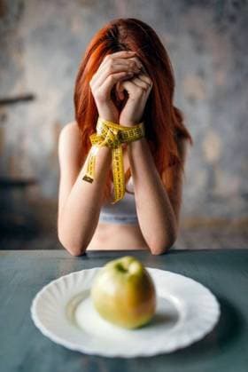 IMAGO Creative: Gesundheit, Magersucht, Bulimie RECORD DATE NOT STATED Womans hands are tied with measuring tape against plate with apple. Fat or calories burning concept. Weight loss