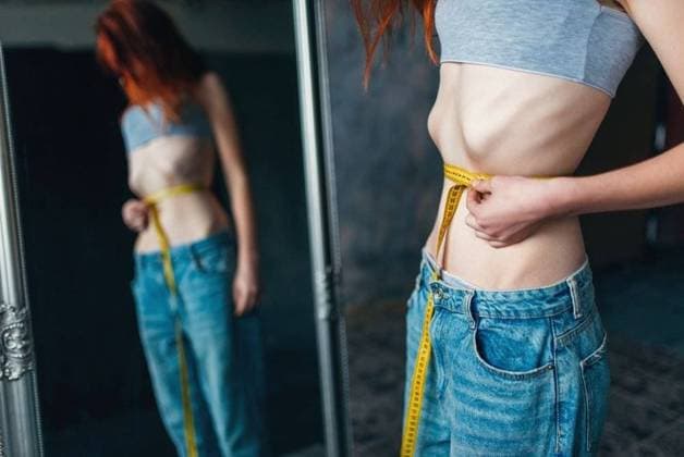 IMAGO Creative: Gesundheit, Magersucht, Bulimie RECORD DATE NOT STATED Thin woman measures her waist against mirror, weight loss, anorexia. Fat or calories burning concept, medical illness