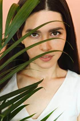 Calm woman with plant in studio Charming female with long hair and brown eyes covering face with palm leaf while standing in studio on pink background and looking at camera Copyright: xZoonar.com DashaxPetrenkox 15964602 ,model released, Symbolfoto ,property released