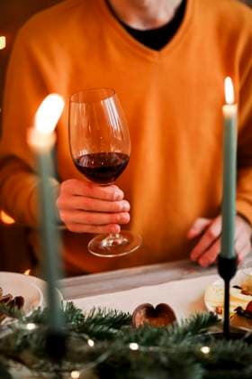 Man in orange sweater holding glass of red wine while celebrating Christmas with family at home Cropped picture of man in orange sweater holding glass of red wine while sitting at table with festive decorations and pair of green burning candles during winter holiday season. Christmas celebration Copyright: xZoonar.com DashaxPetrenkox 17622044 ,model released, Symbolfoto ,property released