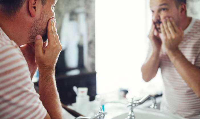 Millennial handsome man looking in mirror, applying moisturizing washing cream Millennial handsome man looking in mirror, applying moisturizing washing cream on cheeks in bathroom, head shot close up. Well groomed young guy doing skincare morning routine Copyright: xZoonar.com DashaxPetrenkox 19686688 ,model released, Symbolfoto ,property released