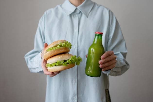 Crop anonymous person in shirt holding appetizing healthy vegan hamburgers with bottle of juice while standing over gray background, Model released, Property released LiliyaSolopova_ID13053_397323_015 Copyright: xLiliyaxSolopovax MR