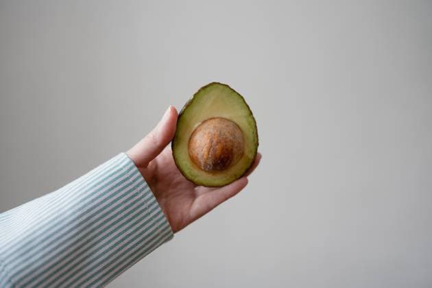 Crop anonymous person with delicious freshly sliced half of ripe avocado pear with seed held against gray background, Model released, Property released LiliyaSolopova_ID13053_397324_016 Copyright: xLiliyaxSolopovax MR
