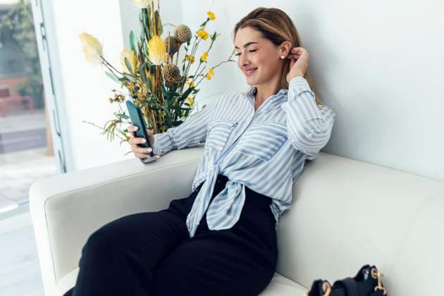 Smiling woman using smart phone sitting on sofa model released, Symbolfoto property released, JSRF02397