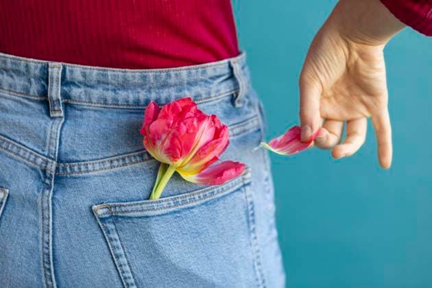 Creative Highlights Symbolbilder Woman plucking petal of tulip from jeans pocket against green background model released, Symbolfoto, AXHF00313