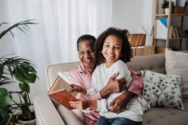 Happy girl holding book sitting with grandmother on sofa at home model released, Symbolfoto property released, EBBF08199