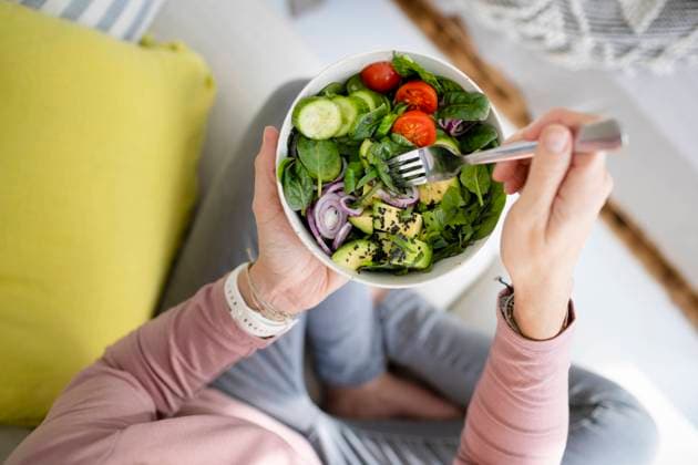 IMAGO Creative, Lifestyle, Tik Tok-Trend thatgirl Hands of woman with bowl of salad sitting on sofa at home model released, Symbolfoto property released, HMEF01523