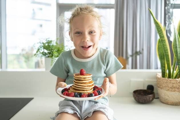 Creative Highlights Symbolbilder Happy girl holding plate of fresh pancakes with berries in kitchen at home model released, Symbolfoto property released, SVKF01329
