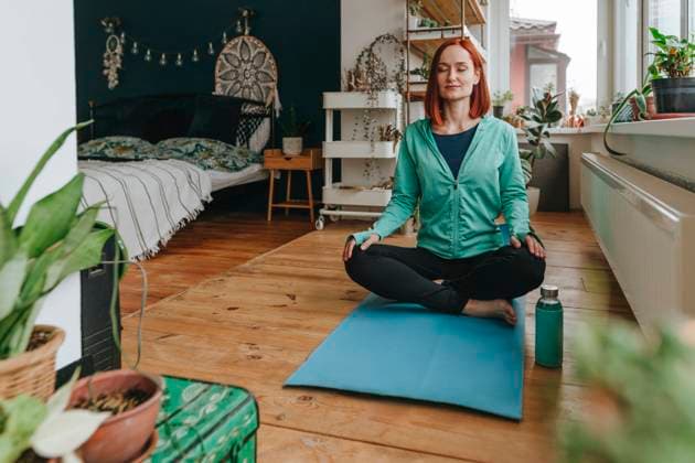 IMAGO Creative, Lifestyle, Tik Tok-Trend thatgirl Smiling woman meditating on exercise mat in bedroom model released, Symbolfoto property released, YTF00553