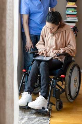 Woman with disability using tablet PC while sitting on wheelchair by caregiver at home Sweden, Stockholm, model released, property released Copyright: xMaskotx , MA100004 MA100004