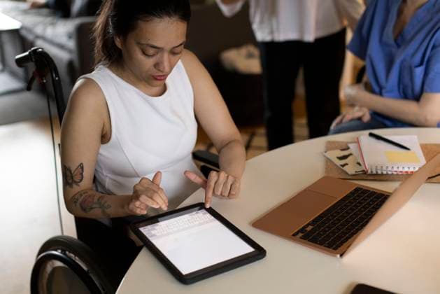 Woman with paraplegia using digital tablet by laptop on dining table at home Sweden, Stockholm, model released, property released Copyright: xMaskotx , MA100039 MA100039