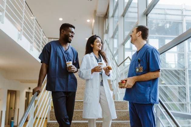 Happy multiracial healthcare workers talking while standing on staircase at hospital Germany, Berlin, model released, property released Copyright: xMaskotx , MA100140 MA100140